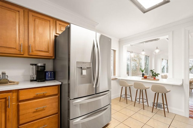 kitchen with light tile patterned floors, ornamental molding, brown cabinets, light countertops, and stainless steel refrigerator with ice dispenser