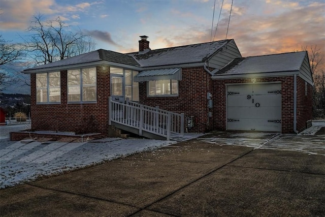 view of front of house featuring a garage, driveway, brick siding, and a chimney