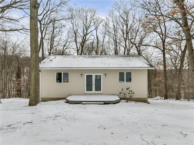 snow covered back of property with french doors and a wooden deck