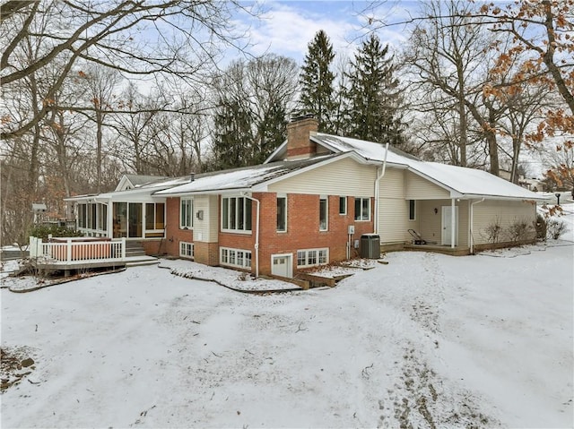 exterior space featuring central air condition unit, a sunroom, a chimney, and brick siding