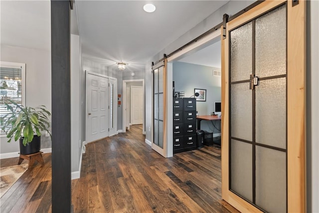 hall with dark wood-style floors, a barn door, and baseboards