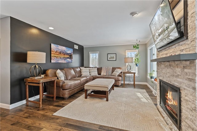 living area with a wealth of natural light, a stone fireplace, baseboards, and wood finished floors