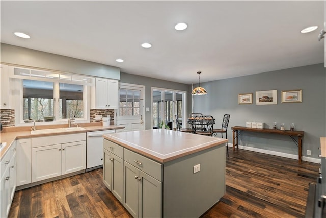 kitchen with a sink, light countertops, a kitchen island, and decorative light fixtures