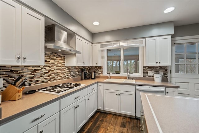 kitchen with a sink, gas stovetop, white cabinets, wall chimney range hood, and dishwasher