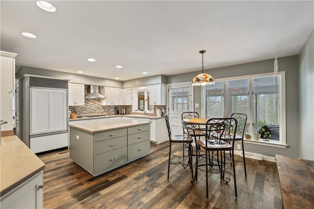 kitchen featuring a center island, decorative light fixtures, light countertops, white cabinets, and wall chimney range hood