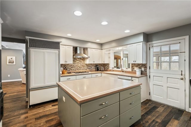 kitchen with a sink, a kitchen island, white cabinets, light countertops, and wall chimney exhaust hood