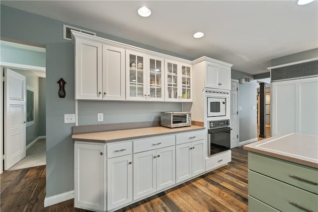 kitchen featuring glass insert cabinets, light countertops, black oven, and white cabinetry