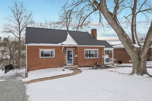 view of front facade with a shingled roof, a chimney, fence, and brick siding