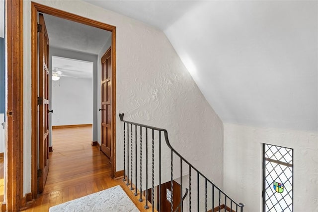 corridor with vaulted ceiling, a textured wall, light wood-type flooring, and baseboards