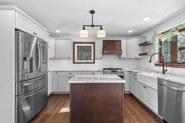 kitchen with custom range hood, hanging light fixtures, appliances with stainless steel finishes, white cabinetry, and light stone countertops