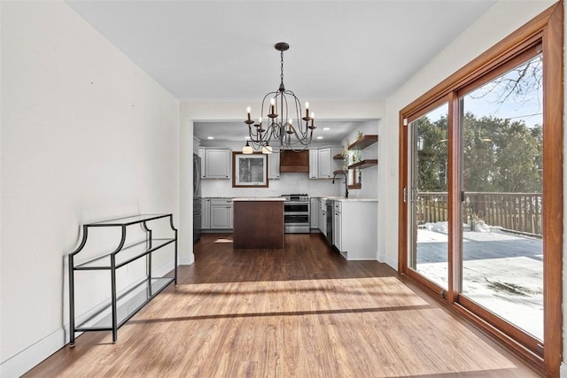 kitchen with dark wood-type flooring, light countertops, appliances with stainless steel finishes, hanging light fixtures, and tasteful backsplash