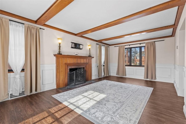 unfurnished living room featuring wainscoting, a fireplace with flush hearth, dark wood-style flooring, beamed ceiling, and a decorative wall