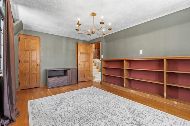 spare room featuring baseboards, wood finished floors, stairs, a textured ceiling, and a chandelier