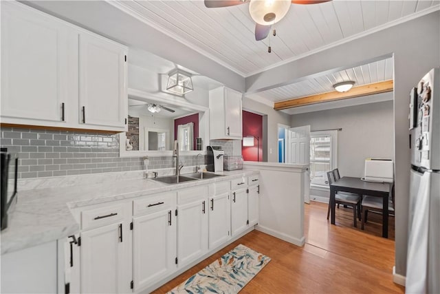 kitchen featuring freestanding refrigerator, a sink, light wood-type flooring, white cabinetry, and backsplash