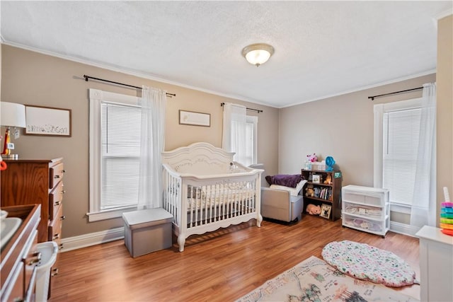 bedroom with a nursery area, a textured ceiling, ornamental molding, and wood finished floors