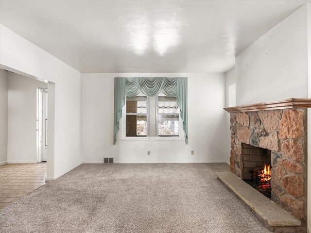 living area with carpet, visible vents, a stone fireplace, and baseboards