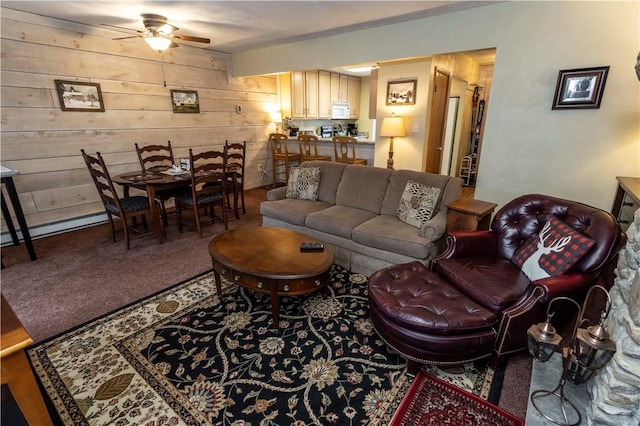 living room with a baseboard heating unit, carpet flooring, ceiling fan, and wooden walls