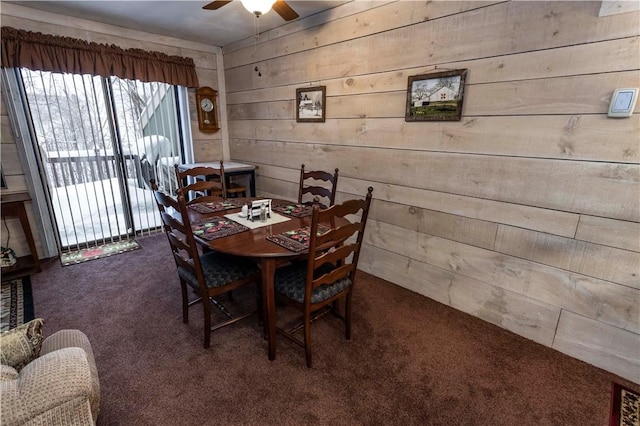 dining area with dark colored carpet, ceiling fan, and wooden walls