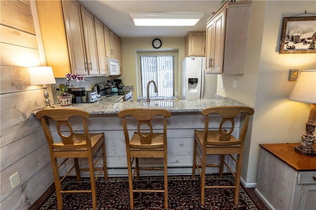 kitchen with white appliances, light stone countertops, a kitchen bar, light brown cabinets, and a sink