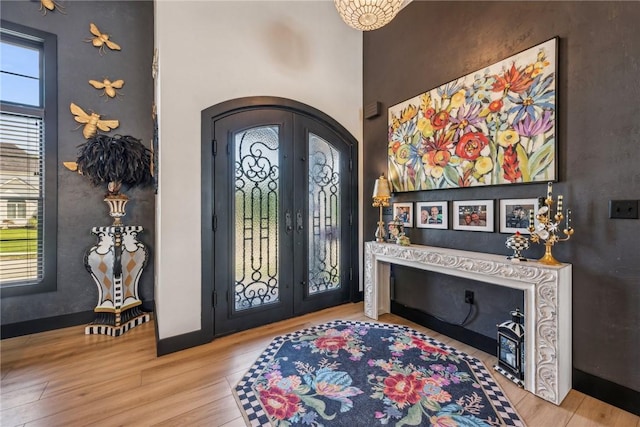 entrance foyer with arched walkways, french doors, baseboards, and light wood-style floors