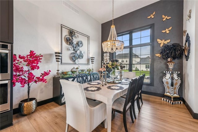dining area featuring baseboards, visible vents, a notable chandelier, and light wood finished floors