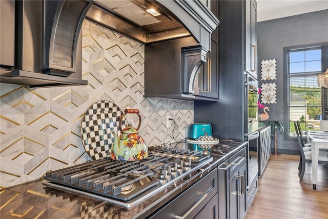 kitchen featuring baseboards, decorative backsplash, dark stone counters, light wood-style floors, and stainless steel gas cooktop