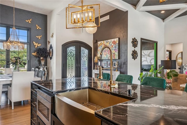 kitchen featuring arched walkways, french doors, stainless steel microwave, an inviting chandelier, and light wood-type flooring