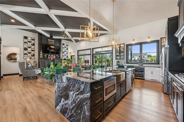 kitchen featuring a center island with sink, wine cooler, appliances with stainless steel finishes, dark stone countertops, and a sink