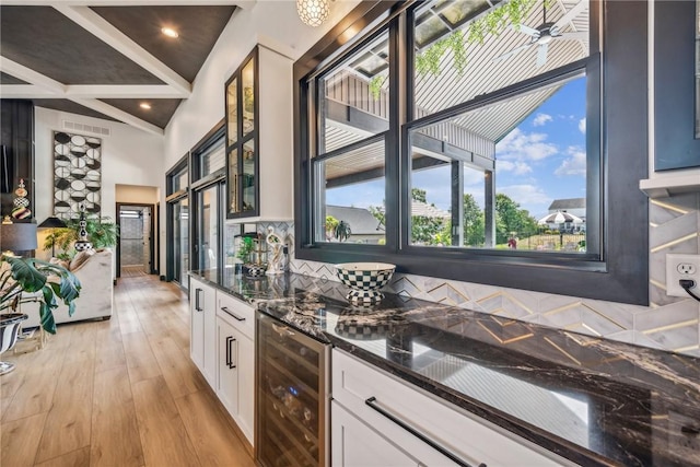 kitchen featuring light wood finished floors, beverage cooler, white cabinets, dark stone counters, and glass insert cabinets