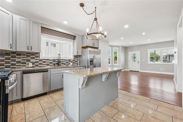 kitchen featuring decorative light fixtures, appliances with stainless steel finishes, open floor plan, a kitchen island, and a sink