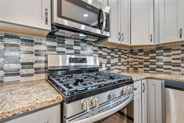 kitchen with white cabinets, appliances with stainless steel finishes, light stone counters, and tasteful backsplash