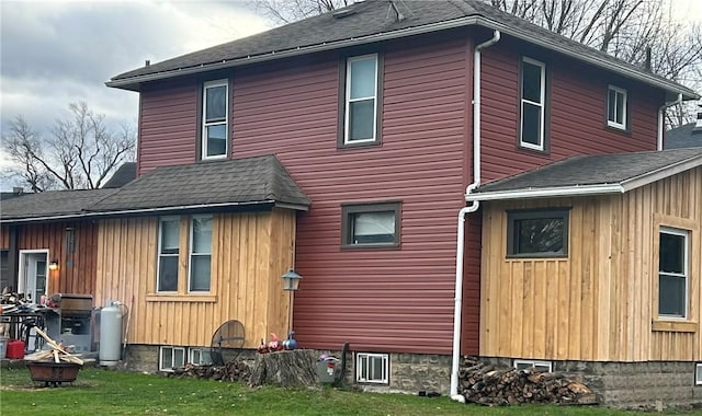 view of side of home featuring roof with shingles, a lawn, and a fire pit