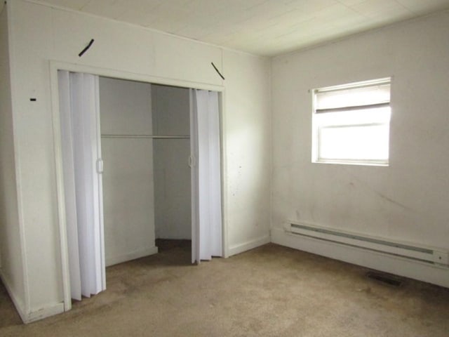 unfurnished bedroom with a baseboard radiator, light colored carpet, and a closet