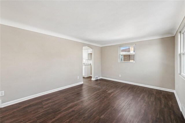 spare room featuring baseboards, arched walkways, and dark wood-type flooring