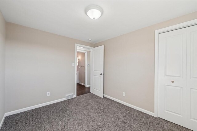 unfurnished bedroom featuring baseboards, visible vents, dark carpet, and a closet
