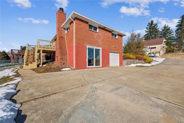 rear view of property with brick siding, a chimney, stairway, driveway, and a wooden deck