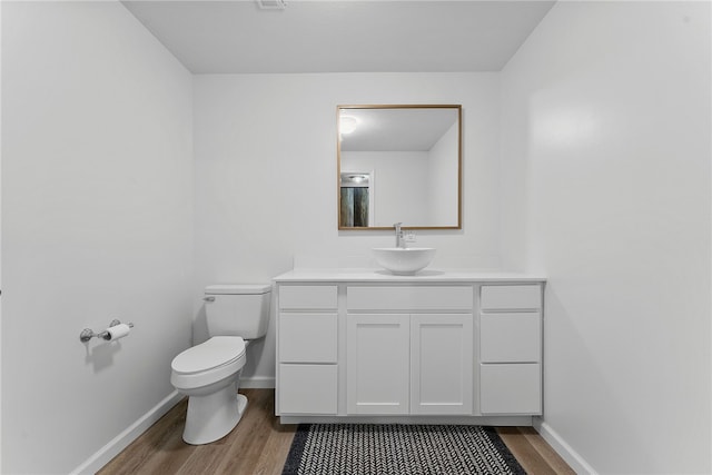 half bathroom with toilet, baseboards, wood finished floors, and vanity