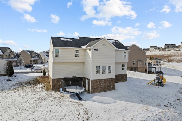 snow covered house with brick siding, a trampoline, a playground, and a residential view