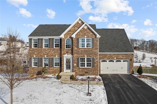 colonial home with a garage, driveway, brick siding, and roof with shingles