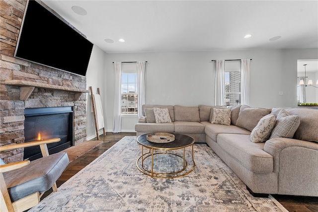 living area featuring dark wood finished floors, a stone fireplace, baseboards, and an inviting chandelier