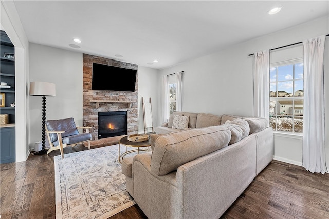 living room with dark wood-style floors, a stone fireplace, and recessed lighting