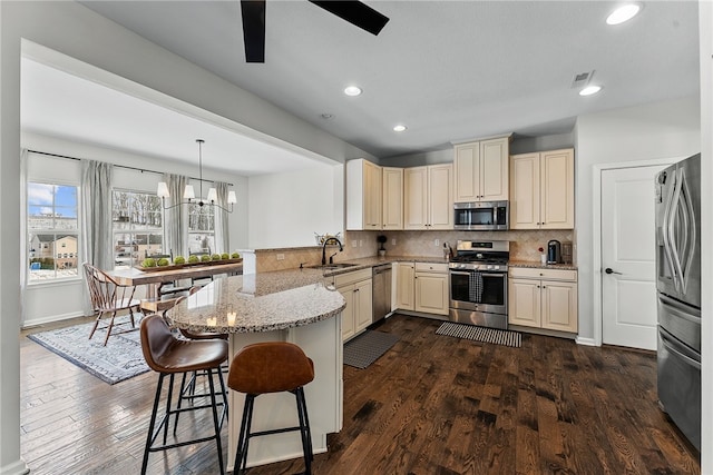 kitchen with light stone counters, a peninsula, a sink, appliances with stainless steel finishes, and pendant lighting