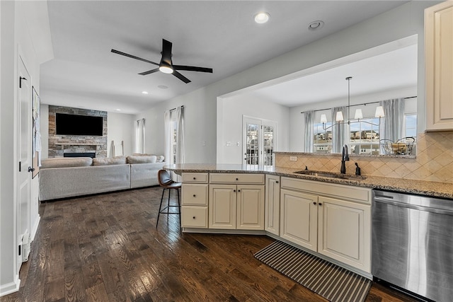 kitchen featuring a sink, open floor plan, hanging light fixtures, stainless steel dishwasher, and light stone countertops