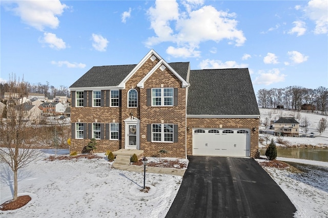 colonial inspired home featuring a garage, driveway, brick siding, and roof with shingles