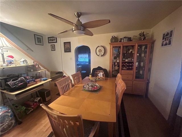 dining space with dark wood-type flooring, arched walkways, and a ceiling fan