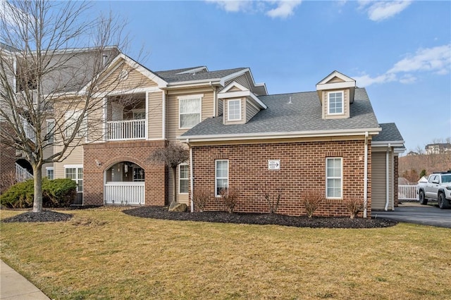 view of front of house featuring a balcony, roof with shingles, a front yard, and brick siding