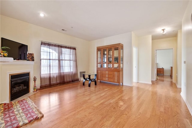 interior space featuring light wood-style floors, a glass covered fireplace, visible vents, and baseboards