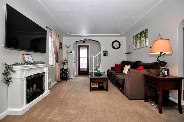 living area with arched walkways, light carpet, a fireplace, and baseboards