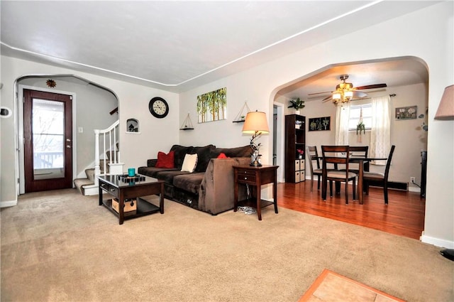 living area featuring a ceiling fan, arched walkways, light colored carpet, and stairs