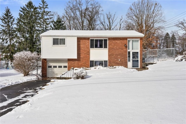 bi-level home with a garage, brick siding, and fence